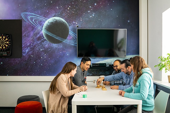 Mitarbeiter sitzen im Pausenraum am Tisch und unterhalten sich über ein Logik-Spiel